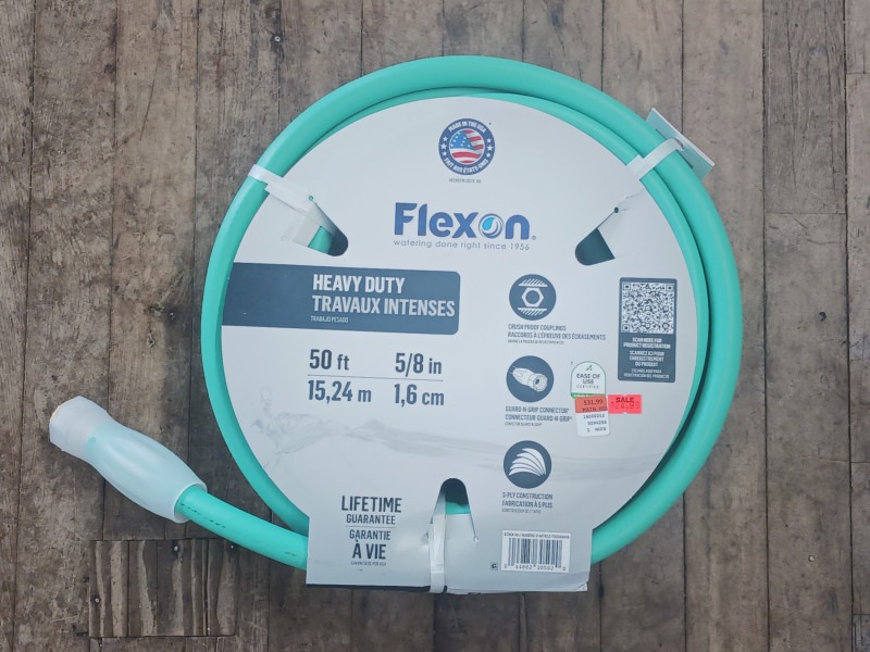 A coiled green garden hose on a wooden floor. The package reads "Flexon Heavy Duty," showing dimensions of 50 ft and 5/8 in. "Lifetime Guarantee" is noted.