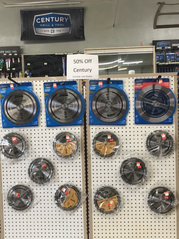 Display of various circular saw blades with a "50% Off Century" sign. Blades are neatly arranged on a pegboard. Industrial, tool store setting.